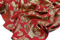 a red and gold scarf with flowers on it, laying on top of a white surface