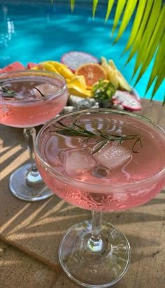 two glasses filled with pink liquid next to a swimming pool