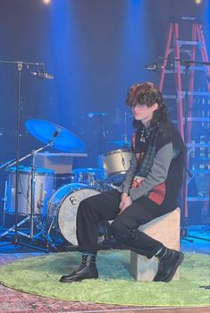 a man sitting on top of a stool next to a drum set in front of a stage