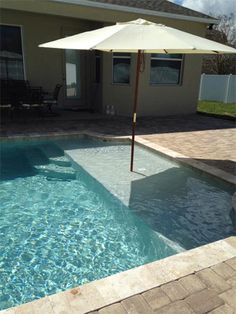 an umbrella sitting on top of a swimming pool next to a house with a patio