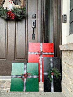 three wrapped presents sitting in front of a door with wreaths on the top and bottom