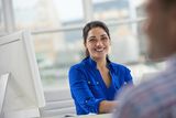 a smiling woman sitting at a table in front of a man who is talking to her