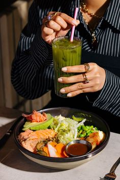 a woman holding a drink over a plate of food with shrimp and lettuce