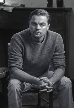 a black and white photo of a man sitting in a chair looking at the camera