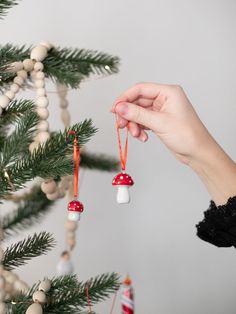 a hand holding two red and white mushrooms ornament hanging from a christmas tree