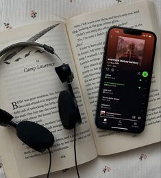 an open book with headphones on it next to a cell phone and earbuds