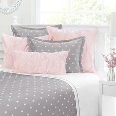 a bed with pink and grey sheets, pillows and pillow cases on top of it