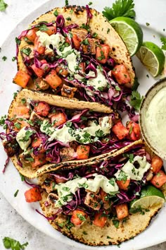 fish tacos with cole slaw and avocado sauce on a white plate