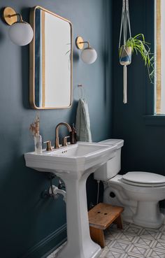 a white toilet sitting next to a sink in a bathroom under a mirror and light fixture