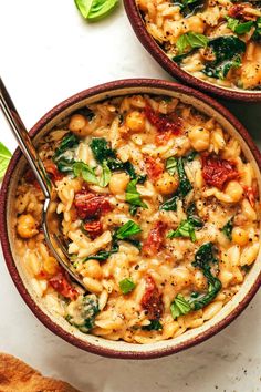 two bowls filled with pasta and spinach on top of a white table next to a spoon