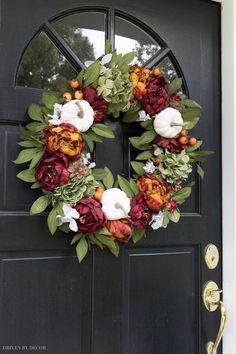 a wreath on the front door with flowers and greenery hanging from it's side