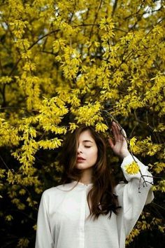 a woman standing in front of a tree with yellow flowers on it's branches