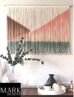 a table with a vase and some plants on it in front of a wall hanging