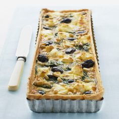 a casserole dish with olives and potatoes in it next to a knife