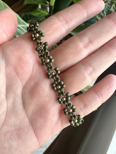 a hand is holding a green beaded bracelet on it's palm, with leaves in the background