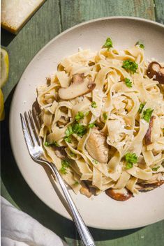 a plate of pasta with mushrooms and parsley on the side next to a fork