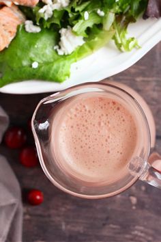 a person is holding a cup of coffee in front of a plate with salad on it