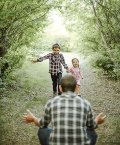 two young children walking down a dirt path in the woods with their hands out to each other