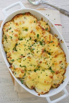 a casserole dish with cheese and parsley in it on a wooden table