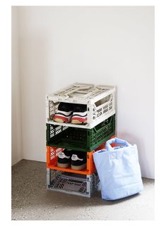 a stack of shoes sitting next to a bag on top of a floor in front of a white wall