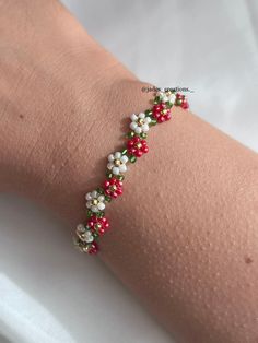 a woman's arm wearing a bracelet with red and white flowers on it,