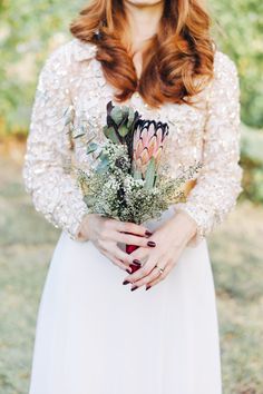 a woman with red hair holding a bouquet of flowers and greenery in her hands