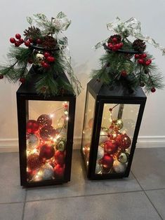 two black lanterns with christmas decorations and lights in them on the floor next to each other