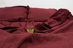 a wine glass sitting on top of a bed covered in red sheets and blankets,