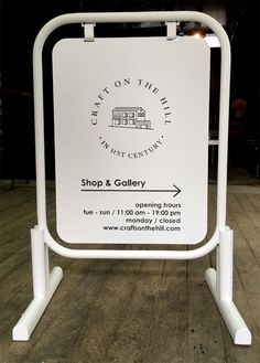 a white sign sitting on top of a wooden floor in front of a store and gallery