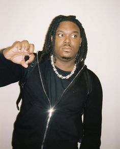 a man with dreadlocks and a black shirt pointing at the camera while wearing a chain around his neck