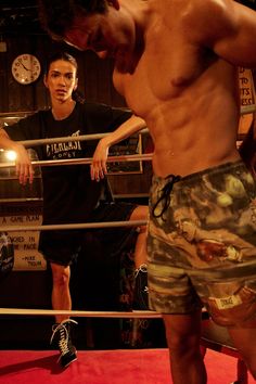 a shirtless man standing in front of a boxing ring next to another male boxer