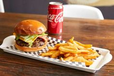 a hamburger and french fries on a tray with a coca - cola can in the background