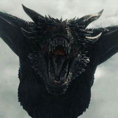 a large black dragon with its mouth open and sharp teeth in front of some clouds