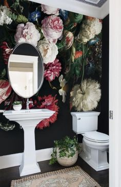 a white toilet sitting under a bathroom mirror next to a wall covered in florals