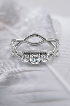 a three stone ring with diamonds on top and an intricate band in the middle, sitting on a white fabric