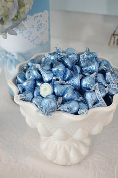 a white bowl filled with blue candies on top of a table next to a vase