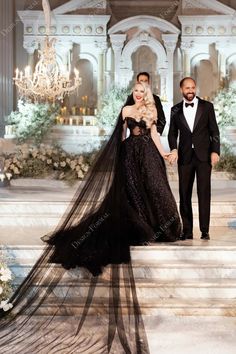 a man and woman in formal wear standing on steps with chandelier behind them