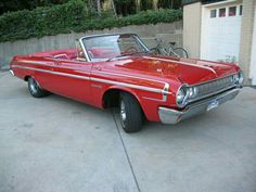 an old red car parked in front of a garage