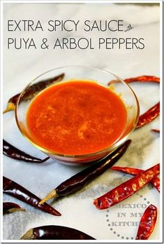 a bowl of red sauce sitting on top of a table next to chili pepper pods