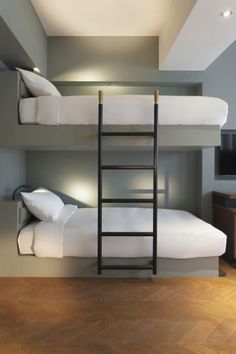 a bunk bed with two white pillows and a ladder to the top, in a room with wood flooring