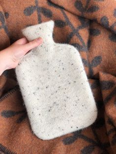 a hand holding a bottle on top of a brown and black patterned blanket that is covered in flecky fabric