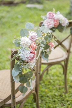 two wooden chairs with flowers and greenery on them sitting in the grass near each other