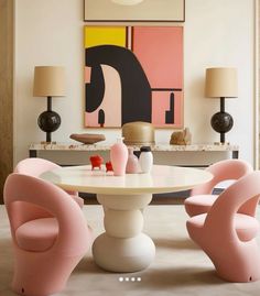 an elegant dining room with pink chairs and art on the wall behind the round table