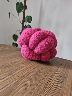 a pink knot sitting on top of a wooden table next to a potted plant