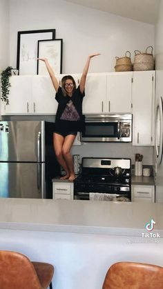 a woman standing in the middle of a kitchen with her arms outstretched and legs spread out