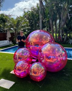 a man standing next to a bunch of shiny balls in front of a swimming pool