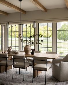 the dining room table is surrounded by chairs and vases with flowers in them, along with large windows