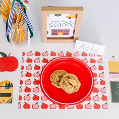 a red plate topped with cookies on top of a table next to an apple and pencils