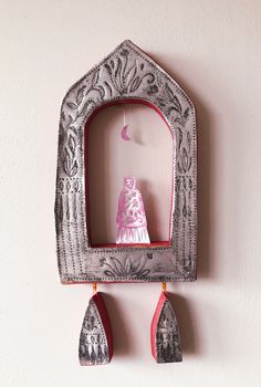 a decorative wall hanging with an ornate frame and two small wooden spoons on it