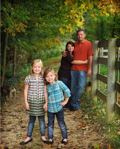 a family standing in front of a fence on a dirt path with trees and grass